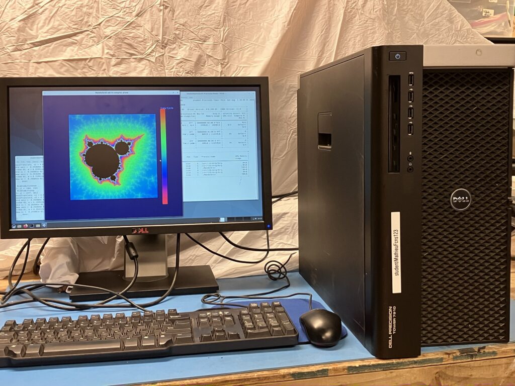 The T7910 tower beside a monitor, keyboard and mouse on a workbench, the screen showing a Mandelbrot set render and terminal output